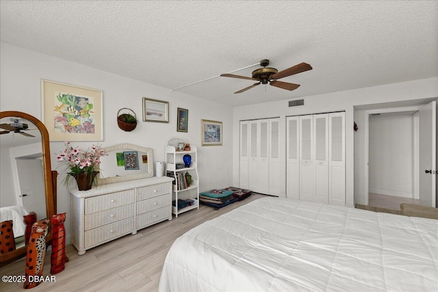 bedroom with ceiling fan, two closets, light hardwood / wood-style flooring, and a textured ceiling