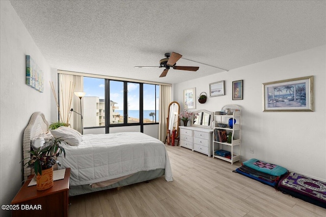 bedroom with a water view, ceiling fan, a textured ceiling, and light wood-type flooring