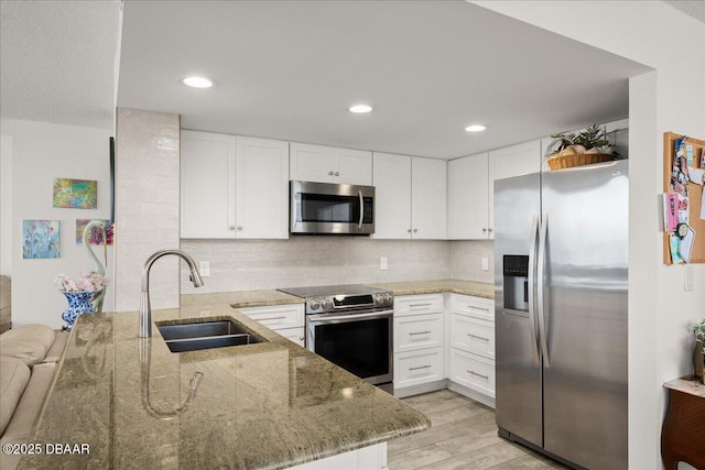 kitchen with sink, stainless steel appliances, light stone countertops, white cabinets, and kitchen peninsula