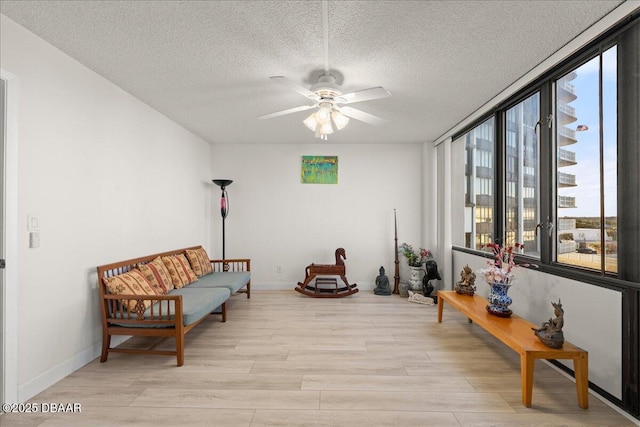 living area with ceiling fan, light hardwood / wood-style flooring, and a textured ceiling