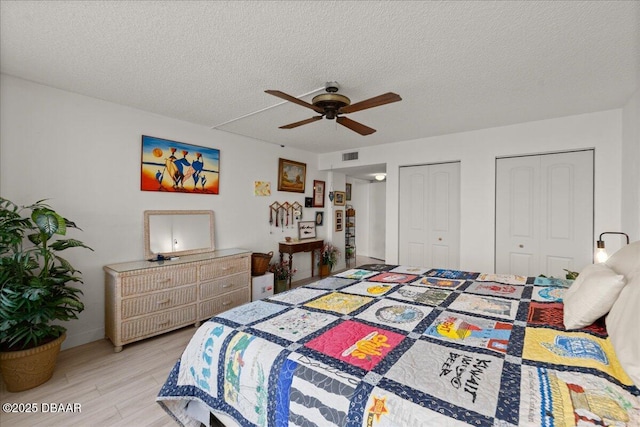 bedroom featuring multiple closets, ceiling fan, a textured ceiling, and light wood-type flooring