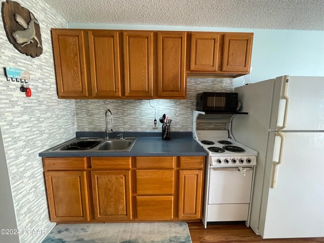 kitchen featuring hardwood / wood-style flooring, sink, a textured ceiling, white appliances, and decorative backsplash