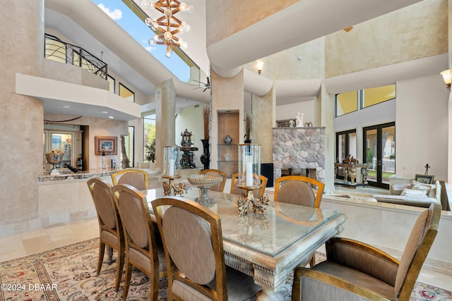 dining area with a stone fireplace, a towering ceiling, a skylight, and an inviting chandelier