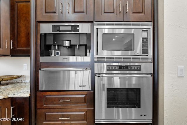 kitchen with light stone countertops, stainless steel microwave, and dark brown cabinets