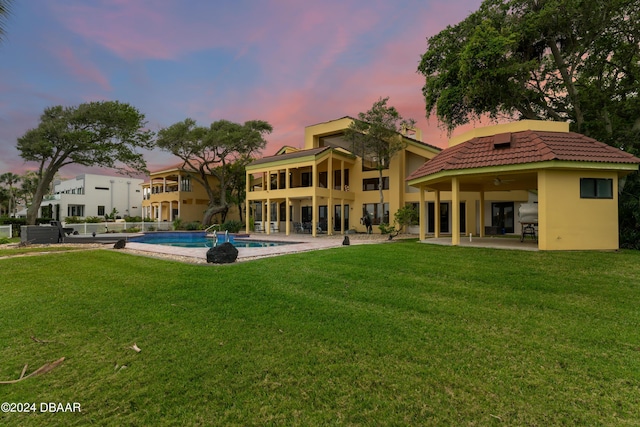 back house at dusk with ceiling fan, a patio area, and a yard