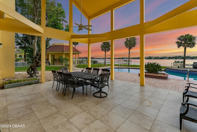 patio terrace at dusk with a fenced in pool, ceiling fan, and a water view