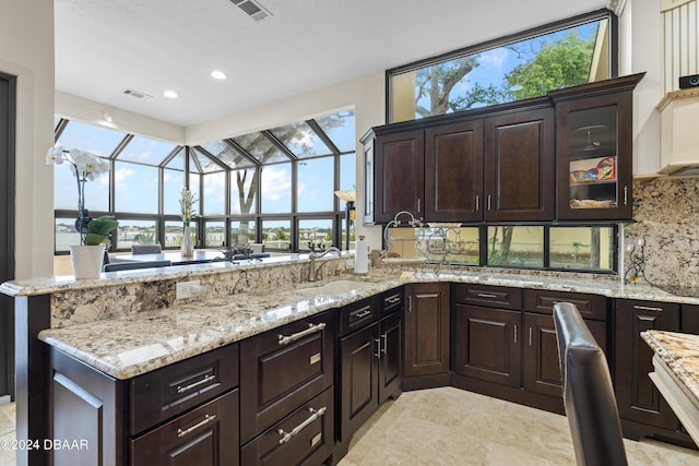 kitchen with decorative backsplash, dark brown cabinets, light stone countertops, and sink