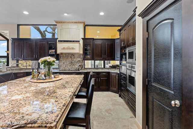 kitchen with a center island, a kitchen breakfast bar, light stone counters, dark brown cabinetry, and stainless steel appliances