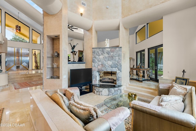 living room with built in features, a high ceiling, a stone fireplace, and ceiling fan