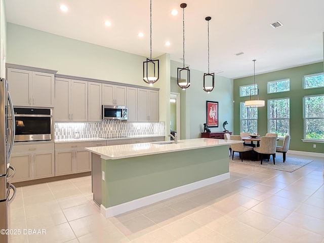 kitchen with visible vents, a towering ceiling, decorative backsplash, appliances with stainless steel finishes, and a sink