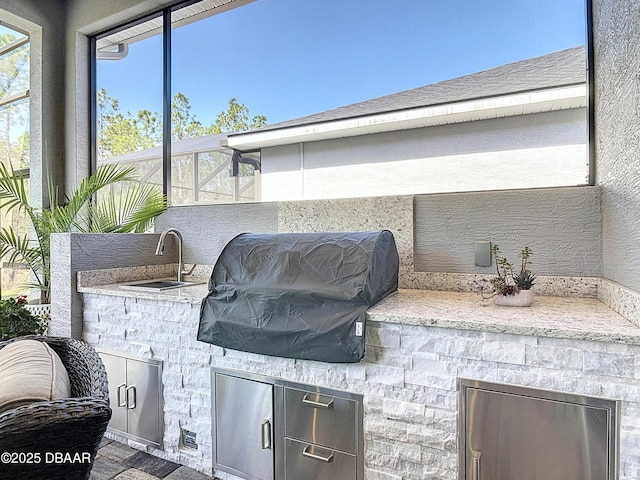 view of patio featuring glass enclosure, exterior kitchen, area for grilling, and a sink