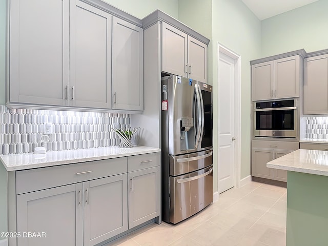 kitchen with light tile patterned floors, stainless steel appliances, decorative backsplash, and gray cabinetry