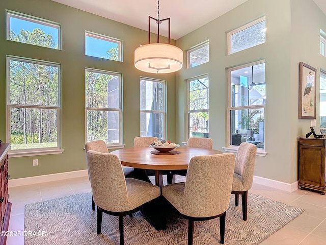 dining room with light tile patterned floors, baseboards, a towering ceiling, and a healthy amount of sunlight