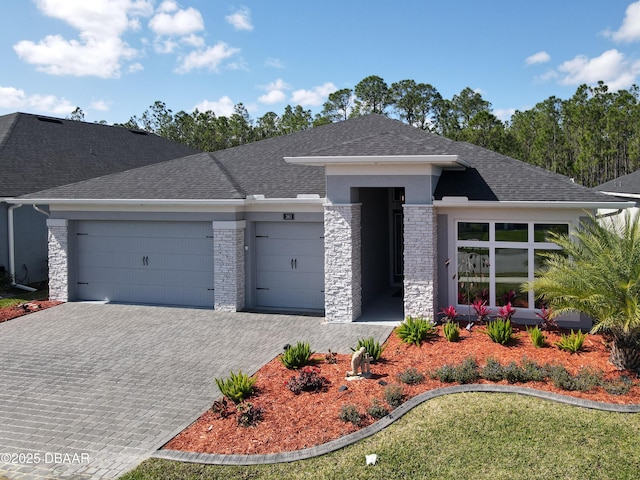 prairie-style house featuring a garage, stone siding, a shingled roof, and decorative driveway