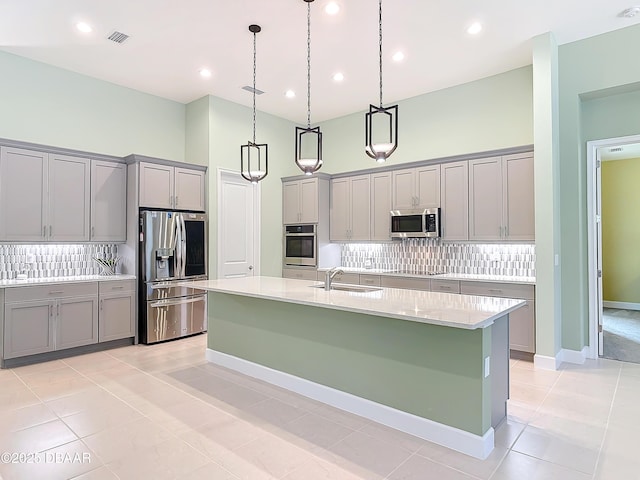 kitchen with appliances with stainless steel finishes, a sink, a towering ceiling, and gray cabinetry