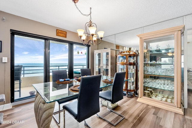 dining space with an inviting chandelier, light hardwood / wood-style flooring, a textured ceiling, and a water view