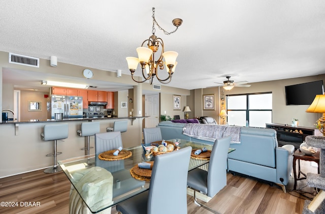 dining area featuring sink, ceiling fan with notable chandelier, a textured ceiling, and light wood-type flooring