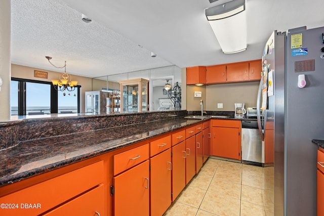 kitchen with light tile patterned floors, appliances with stainless steel finishes, dark stone countertops, an inviting chandelier, and a textured ceiling