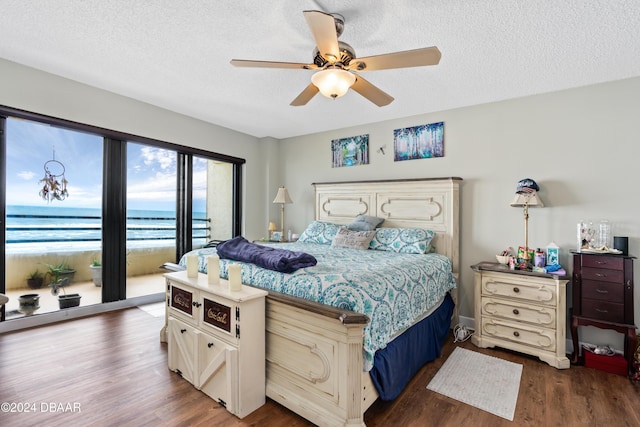 bedroom featuring ceiling fan, dark hardwood / wood-style floors, a textured ceiling, and a water view