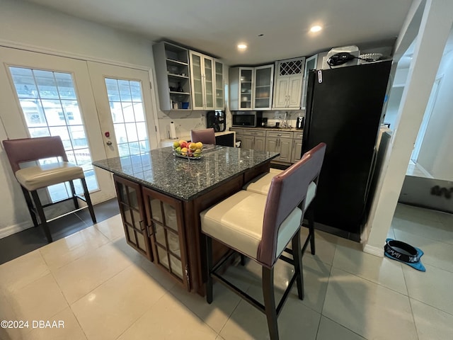 kitchen featuring dark stone countertops, black refrigerator, french doors, and light tile patterned floors