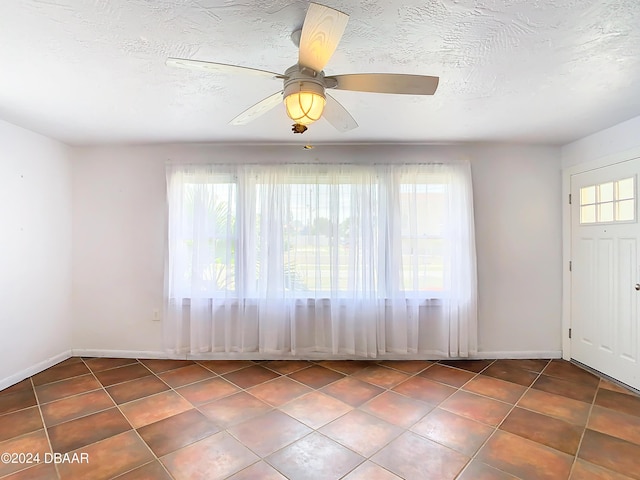 tiled empty room with a ceiling fan, a textured ceiling, and baseboards