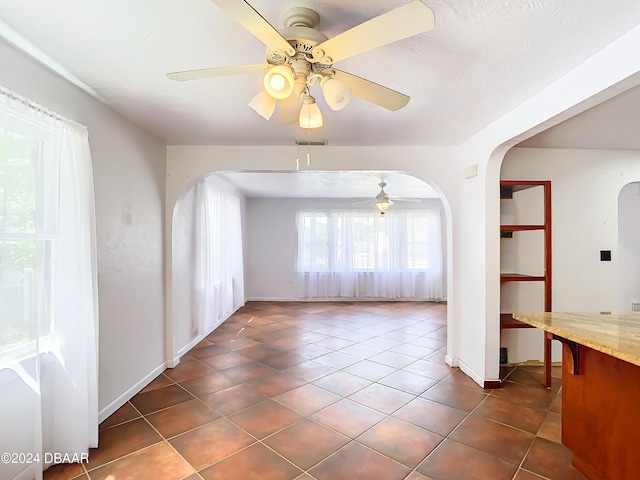 unfurnished room with visible vents, arched walkways, baseboards, ceiling fan, and dark tile patterned floors