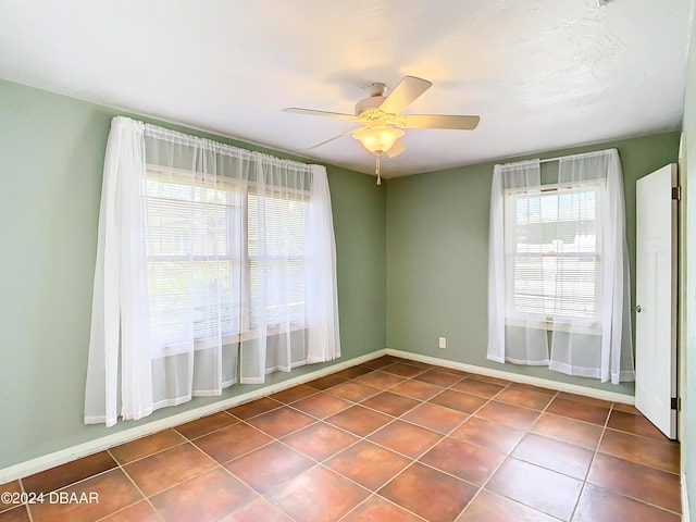 empty room featuring dark tile patterned floors, baseboards, and a ceiling fan