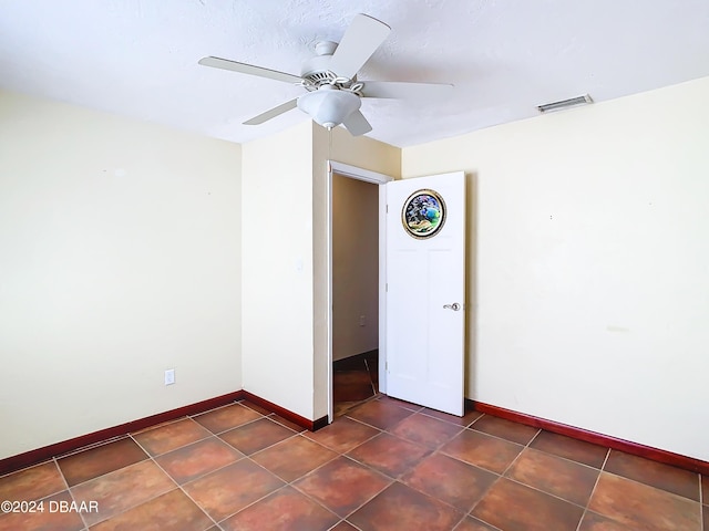 spare room featuring ceiling fan, dark tile patterned flooring, visible vents, and baseboards