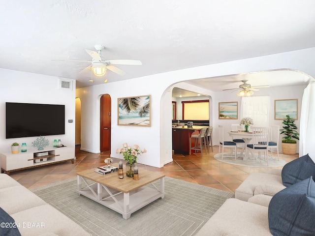 living area with ceiling fan, visible vents, arched walkways, and tile patterned floors