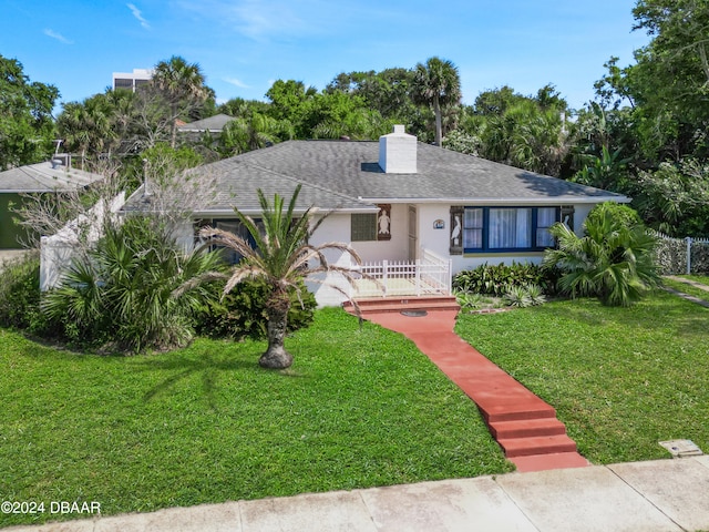 view of front of home with roof with shingles, a chimney, a front lawn, and stucco siding