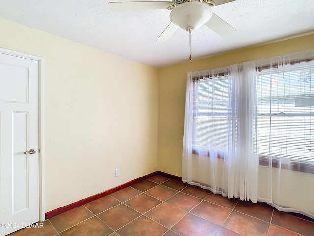 unfurnished room featuring a ceiling fan, dark tile patterned flooring, and baseboards