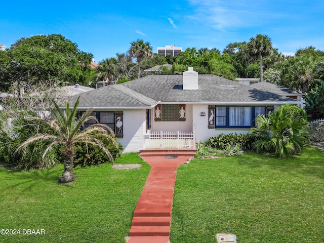 ranch-style home with roof with shingles, a chimney, a front lawn, and stucco siding