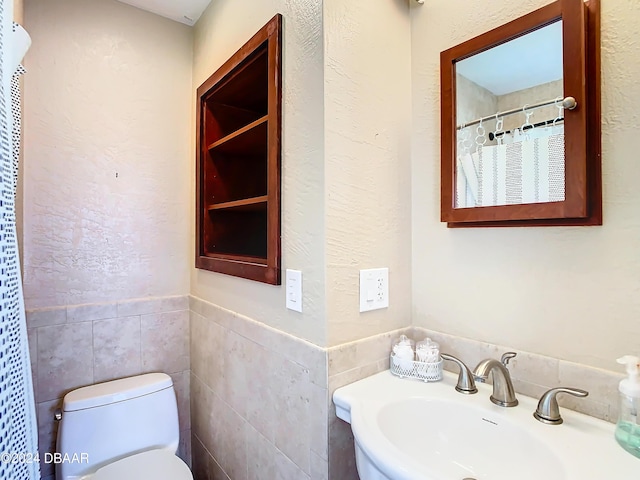 bathroom with tile walls, a textured wall, toilet, a sink, and a shower with curtain