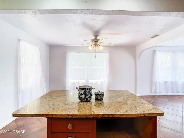 kitchen with ceiling fan, light stone counters, tile patterned floors, and a center island