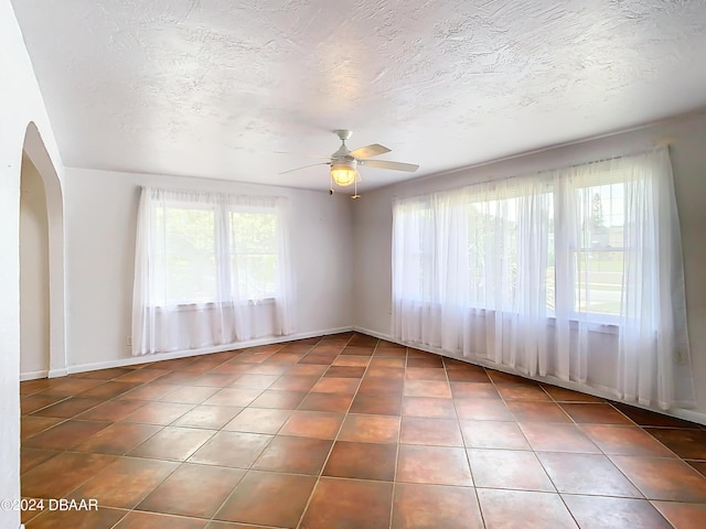 tiled spare room with arched walkways, ceiling fan, and a textured ceiling