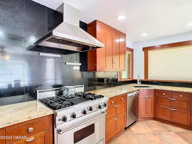 kitchen featuring brown cabinets, wall chimney range hood, stainless steel appliances, and a sink