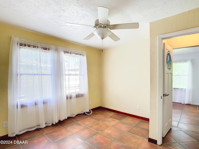 tiled empty room with a ceiling fan, baseboards, and a textured ceiling