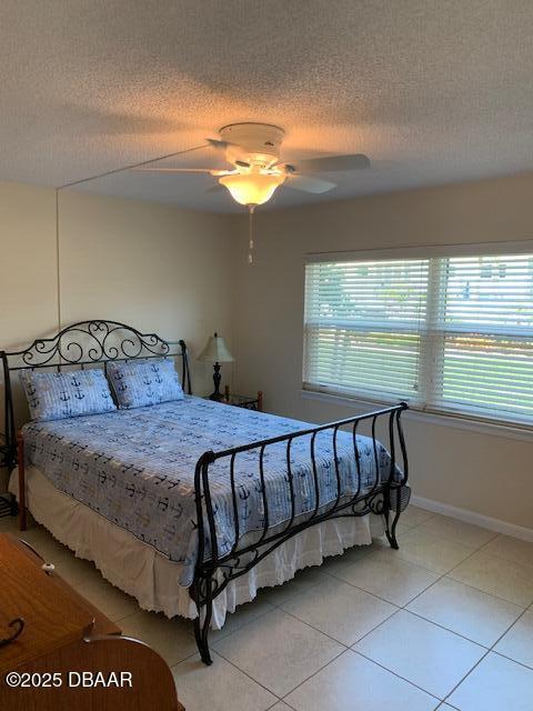 325 Causeway Cswy N Unit D104, New Smyrna Beach, FL 32169 - bedroom featuring light tile patterned flooring, baseboards, a ceiling fan, and a textured ceiling