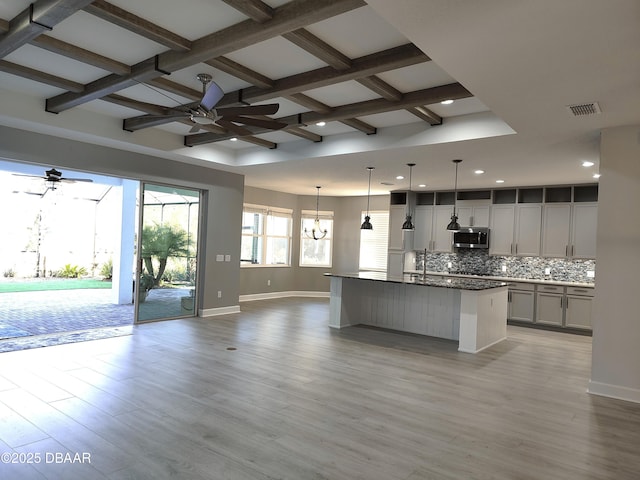 kitchen with pendant lighting, ceiling fan with notable chandelier, decorative backsplash, and a center island with sink