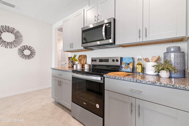 kitchen with stone countertops, light tile patterned floors, white cabinets, and appliances with stainless steel finishes