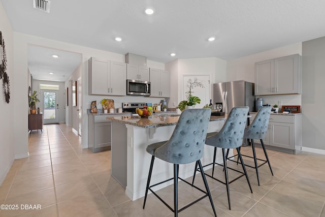 kitchen with a breakfast bar area, gray cabinetry, dark stone countertops, stainless steel appliances, and a kitchen island