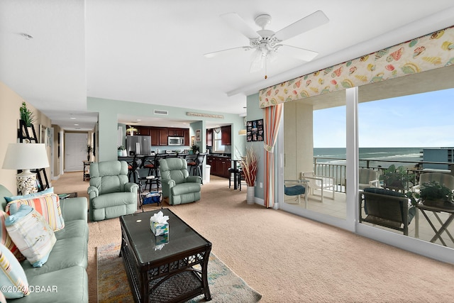 carpeted living room with ceiling fan and a water view