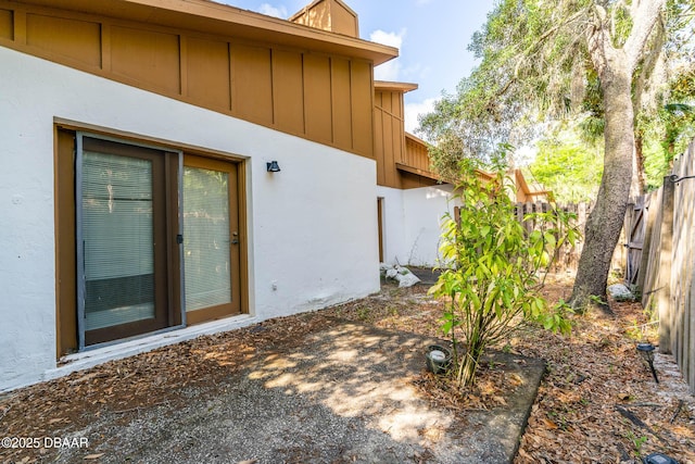 exterior space featuring stucco siding, board and batten siding, and fence