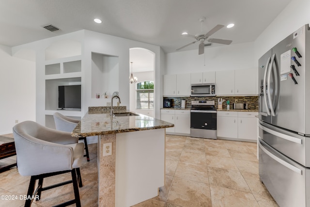 kitchen with stainless steel appliances, stone countertops, white cabinetry, sink, and decorative backsplash