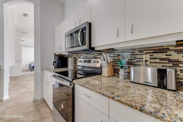 kitchen featuring stainless steel appliances, light tile patterned floors, backsplash, light stone countertops, and white cabinetry