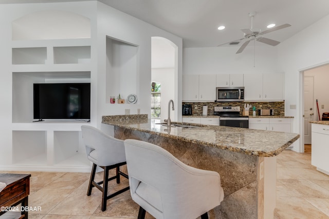 kitchen with stainless steel appliances, kitchen peninsula, sink, a breakfast bar area, and white cabinetry