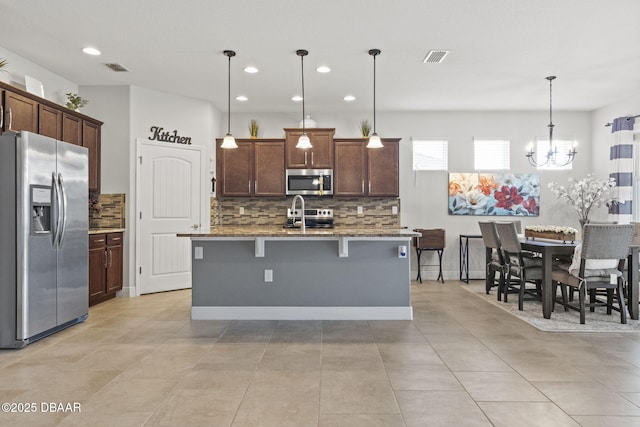 kitchen with a breakfast bar, stone countertops, decorative light fixtures, stainless steel appliances, and a kitchen island with sink