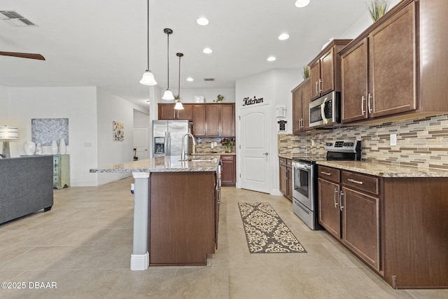 kitchen with sink, appliances with stainless steel finishes, decorative backsplash, a center island with sink, and decorative light fixtures