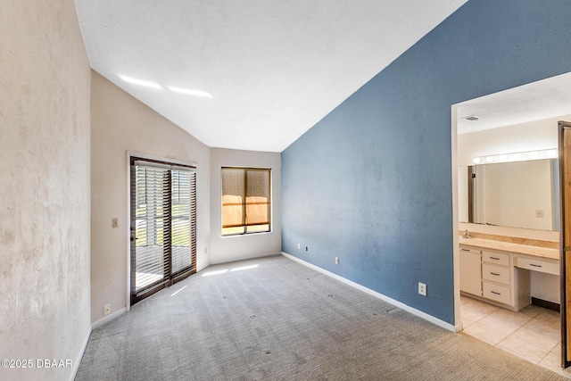 unfurnished bedroom featuring vaulted ceiling, built in desk, connected bathroom, access to outside, and light carpet