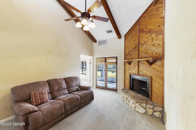 carpeted living room featuring beamed ceiling, ceiling fan, a stone fireplace, and high vaulted ceiling